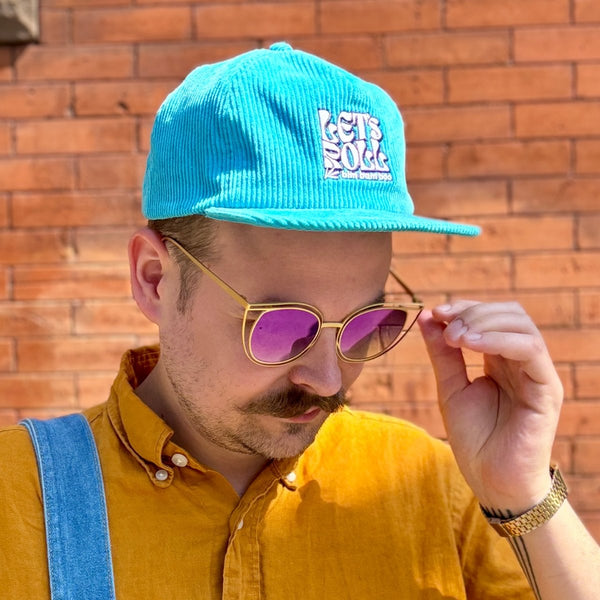 A person is wearing a teal corduroy baseball  cap with the words