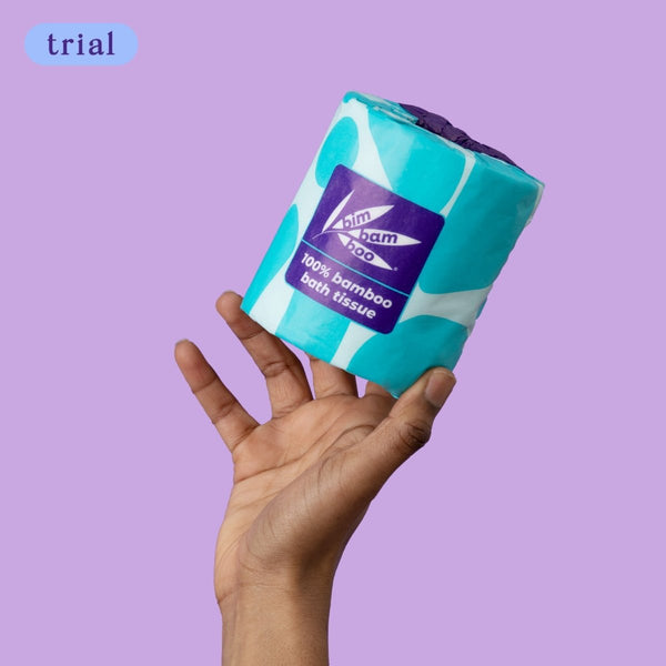 Hand holding a roll of bamboo toilet tissue against a purple background