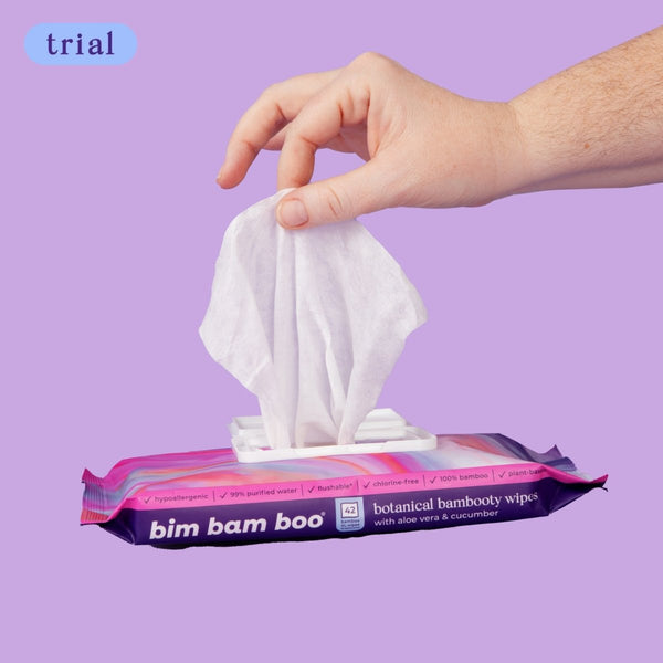 Hand pulling a wipe from bim bam boo package on purple background.