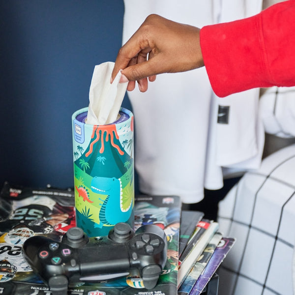 Hand pulling tissue from colorful tissue box next to gaming controller on table.