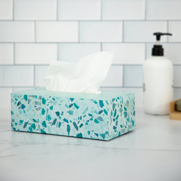 Tissue box on a marble countertop with tile wall and soap dispenser in the background