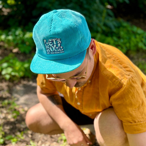 A person is wearing a teal corduroy baseball  hat with the words 